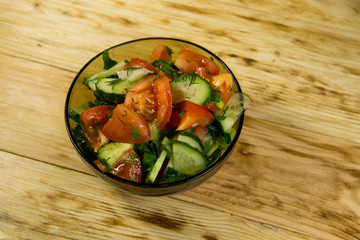 Fresh salad with tomato, cucumber, onion, parsley and dill in glass bowl on wooden table