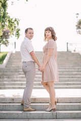 beautiful couple on a walk, the girl in the beige dress and the guy in bright clothes standing on the stairs, holding hands, Park, summer, nature