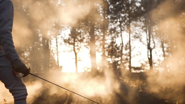 Male and female fencing in the forest wearing full outfit. Footage in slowmotion with sunflare and haze