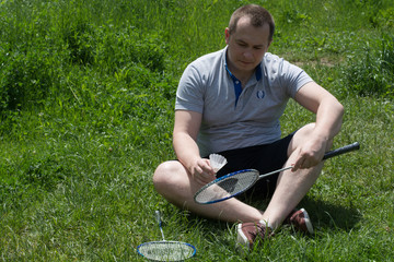 Naklejka na ściany i meble Young, handsome man holds badminton rocket and shuttlecock on grass - healthy lifestyle