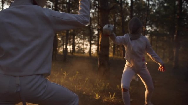 Two sportsmen in outfit and masks fencing in forest in slowmotion. Sun flare and gaze