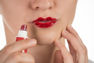 Naklejka premium A beautiful young girl applies a persistent liquid red lipstick from a tube to her lips, and then takes it off as a film