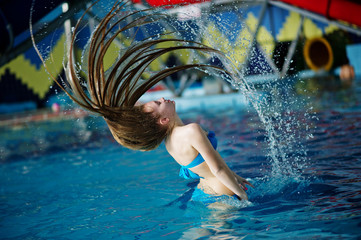 Motion freeze on a beautiful young girl splashing the pool water with her hair in the water park.