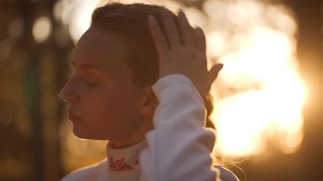 Concentrated Caucasian beautiful female putting on a fencing mask in slowmotion. Footage with sun flare