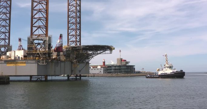Jack up rig Atlantic Rotterdam, Three-Legged Self Elevating Unit drilling platform,  berthed in Haringhaven. Tug Triton sailing by. IJMUIDEN, THE NETHERLANDS - MAY 2017