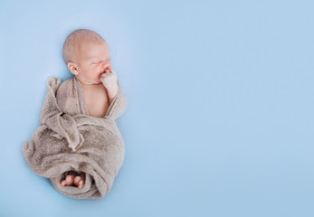 Studio shoot of cute 10 days old newborn baby sleeping on a soft blue blanket in a wrap