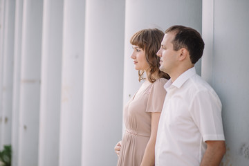 Fototapeta premium a love story, a man and a woman wearing light clothes, standing near a grey wall, profile, hug, family, a date, a walk