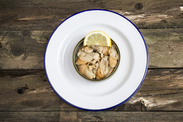 Can of preserved with clams on a plate on a rustic wooden table.
