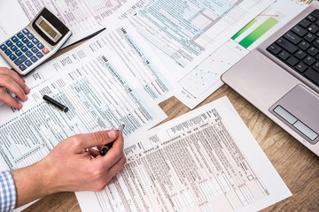 Naklejka premium Businessman filling 1040 tax form with help laptop at office desk