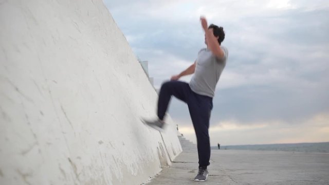 Young Caucasian male gymnast jumping from wall and doing back somersault using thrusting off the wall in slowmotion