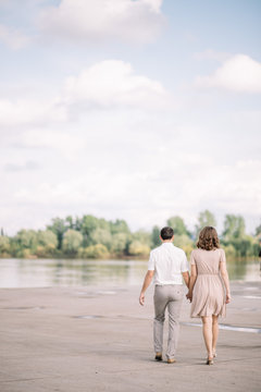 love story, beautiful couple a man and a woman in bright clothes, dress walking by the river, going to the beach, rear view, vertical, blue sky with white clouds, summer, nature