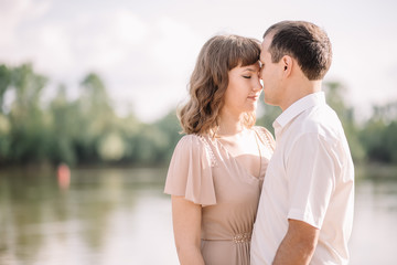 Obraz premium love story, beautiful couple a man and a woman in bright clothes, happy family, walking along the river Bank,are holding hands, cuddling, summer, nature