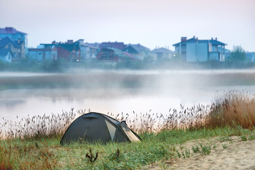 Green tent near river with morning mist