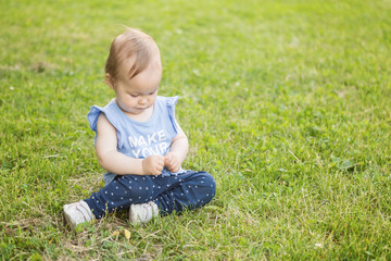 Fourteen months old baby girl sitting on the grass on the sunny summer day