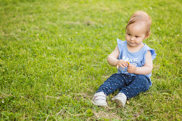 Fourteen months old baby girl sitting in the shadow on the grass on the sunny summer day