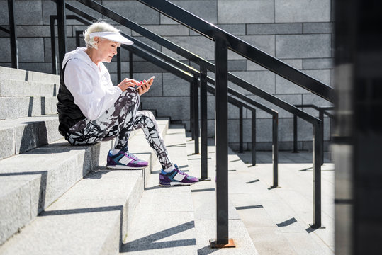 Concentrated aged lady messaging through her cellphone on stone steps