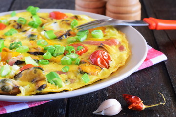 Omelet with mussels, cherry tomatoes and green onions on a ceramic plate on a black background. Healthy breakfast concept