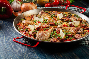 Traditional paella with chicken legs, sausage chorizo and vegetables served in paellera