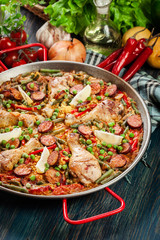 Traditional paella with chicken legs, sausage chorizo and vegetables served in paellera