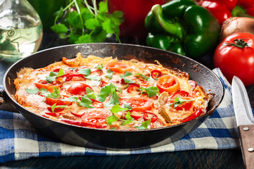 Frittata made of eggs, sausage chorizo, red pepper, green pepper, tomatoes, cheese and chili in a pan on wooden table