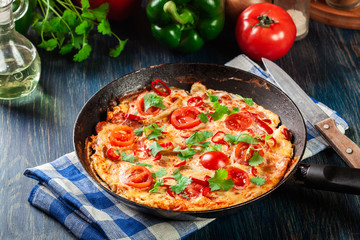 Frittata made of eggs, sausage chorizo, red pepper, green pepper, tomatoes, cheese and chili in a pan on wooden table