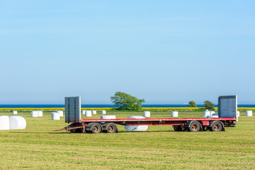 Empty truck trailer parked in a field full of silage bales. The bales are to be loaded on the trailer for later transport.