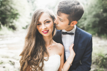 Beautifull wedding couple kissing and embracing near the shore of a mountain river with stones