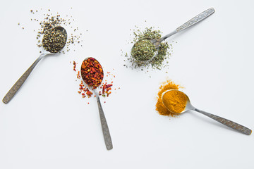 Top view of assorted aromatic spices in metal spoons isolated on white