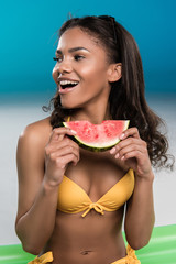 young african american woman in swimsuit eating watermelon