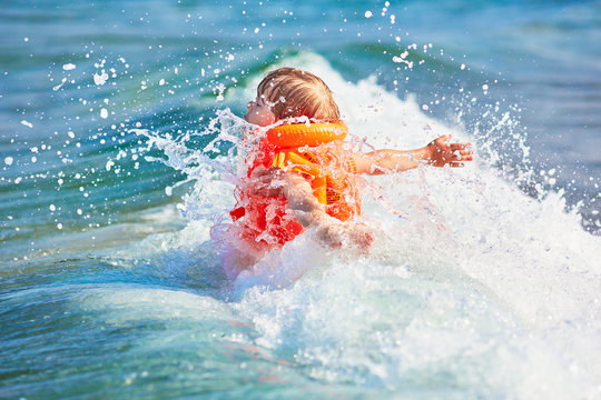 Little boy in orange life vest swimming in wave sea (selective DOF)