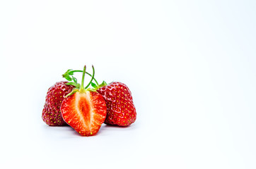 Two whole ripe strawberry berries and a cut berry in the foreground.