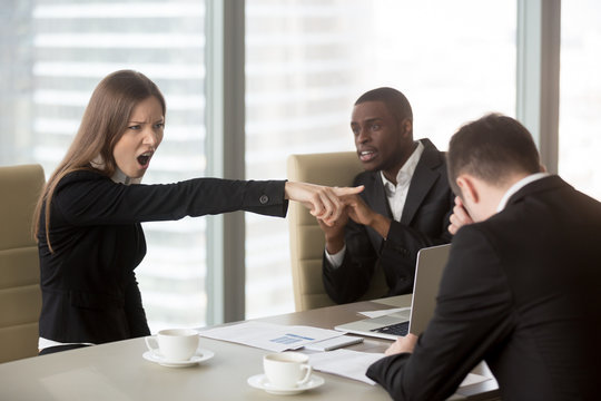 Angry female furious boss scolding employee at mixed-race team meeting, firing dismissing depressed office worker for failure, bad work results, being ineffective, pointing finger, its your fault