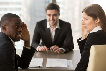 Multiracial confused employers covertly discuss job applicant, hide face with hands, look puzzled...