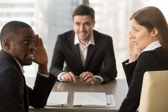 Multiracial confused employers covertly discuss job applicant, hide face with hands, look puzzled bewildered, secretly whisper during failed interview, bad negative first impression, make decision