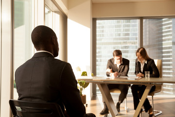 Back view at african-american applicant waiting for result after job interview while employers or...