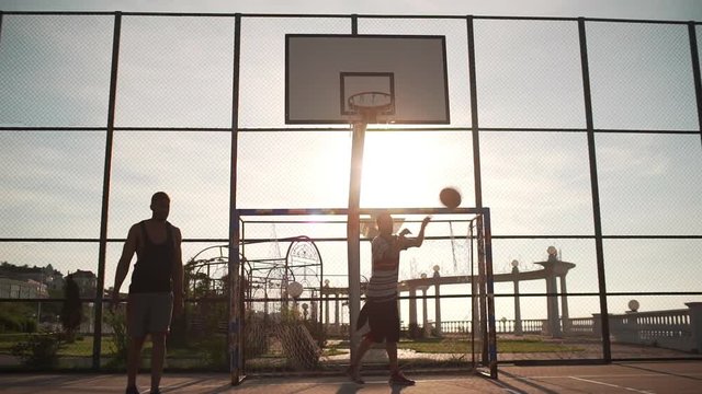Young active people playing streetball on beautiful outdoor sports ground. Footage in slowmotion with beautiful sun flare