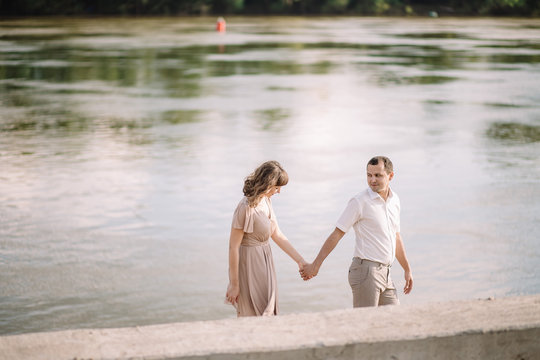 a beautiful couple, a girl with a guy in summer clothes, dress beige, are on the river Bank, holding hands, nature