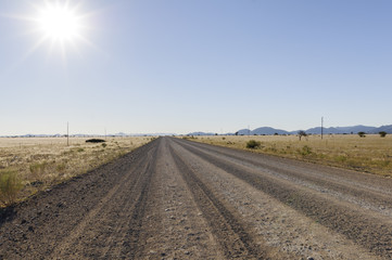 Fototapeta na wymiar Landschaft mit gerader Strasse und Sonne / Landschaft mit gerader Strasse bis zum Horizont und Sonne, Namibia, Afrika.