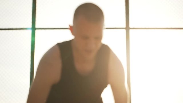 Close up footage of Caucasian male dribbling playing streetball on outdoor sports ground. Footage in slowmotion with sun flare