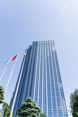 青空にそびえる日本の高層オフィスビルと国旗｜ビジネス街・企業本社・グローバル経済イメージ