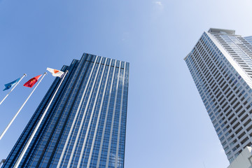 青空にそびえる日本の高層オフィスビルと国旗｜ビジネス街・企業本社・グローバル経済イメージ