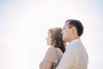 beautiful couple, the girl in the beige dress, the man in white shirt standing close to each other on the background of sky, sun, close-up, summer, heat, nature, love story