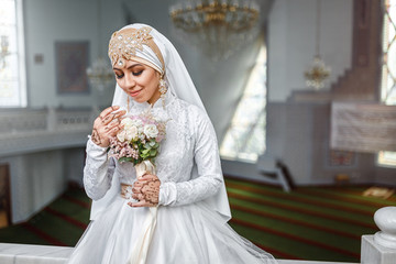 Muslim bride with jewelery in a headscarf hijab with a bouquet of flowers in a mosque