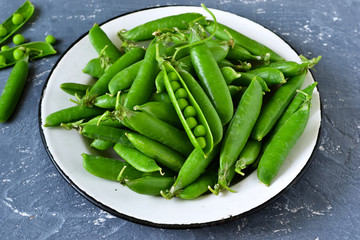 Fresh, young green peas in a plate on a concrete background. Bio food background.