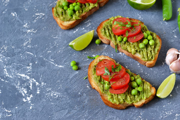 Toasts with avocado, green peas and tomatoes on a concrete background. Lunch and snack.