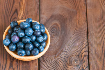 Heap of fresh raw blueberries in a wooden plate. Wooden background. Copy space and close up.