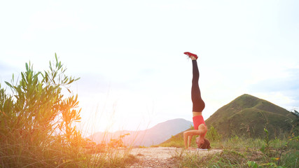 Young woman practicing yoga headstand on top of rock. Landscape mountain view.