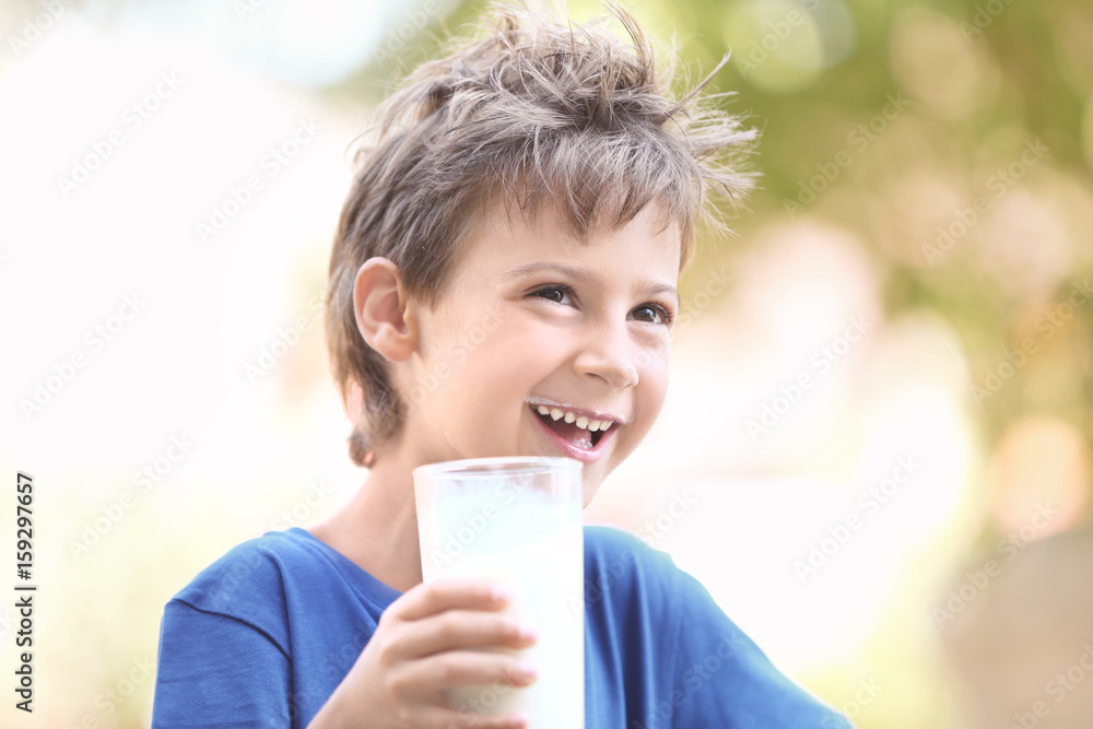 Wall mural cute boy in blue shirt holding glass of milk on blurred background