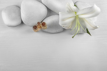 Spa stones, beautiful lily and bottles with aroma oil on white wooden background