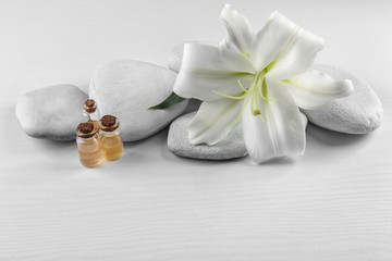 Fototapeta na wymiar Spa stones, beautiful lily and bottles with aroma oil on white wooden background